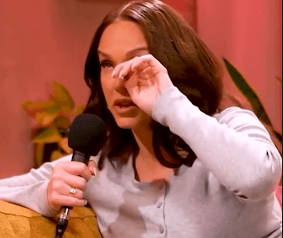 Woman wiping away tears while holding a microphone.