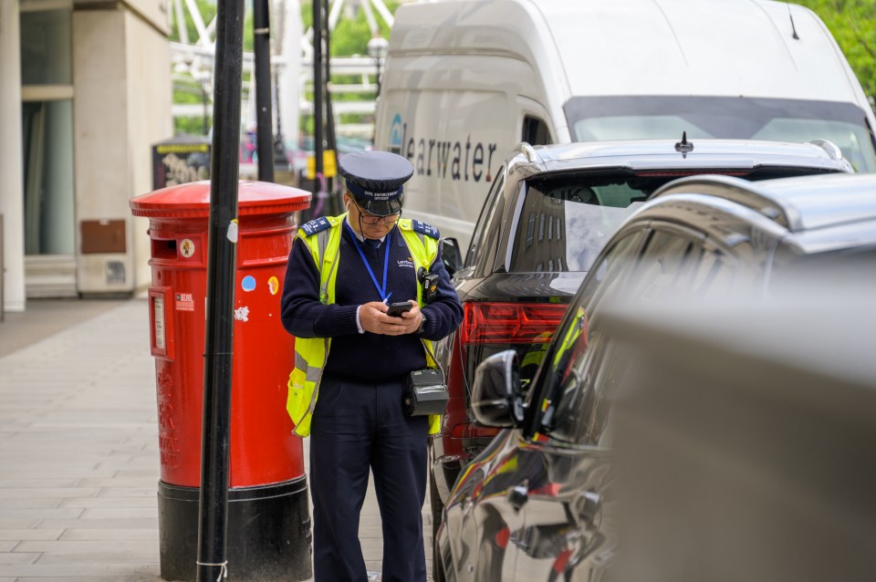 Traffic warden uses smartphone next to traditional red British Post Box.