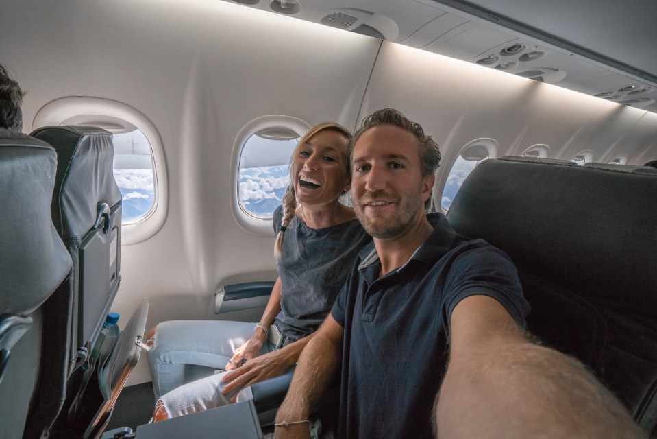 Young couple in airplane using mobile phone during flight to take selfie portrait<br />
People travel technology concept