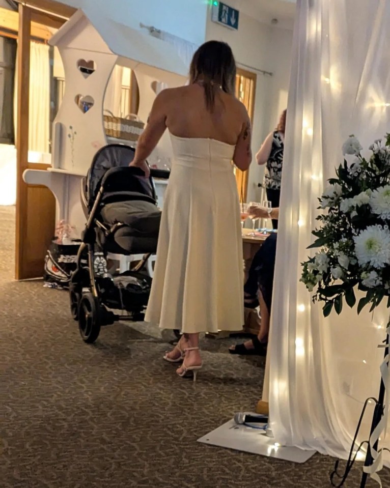 A woman in a white dress pushes a baby stroller at a wedding reception.