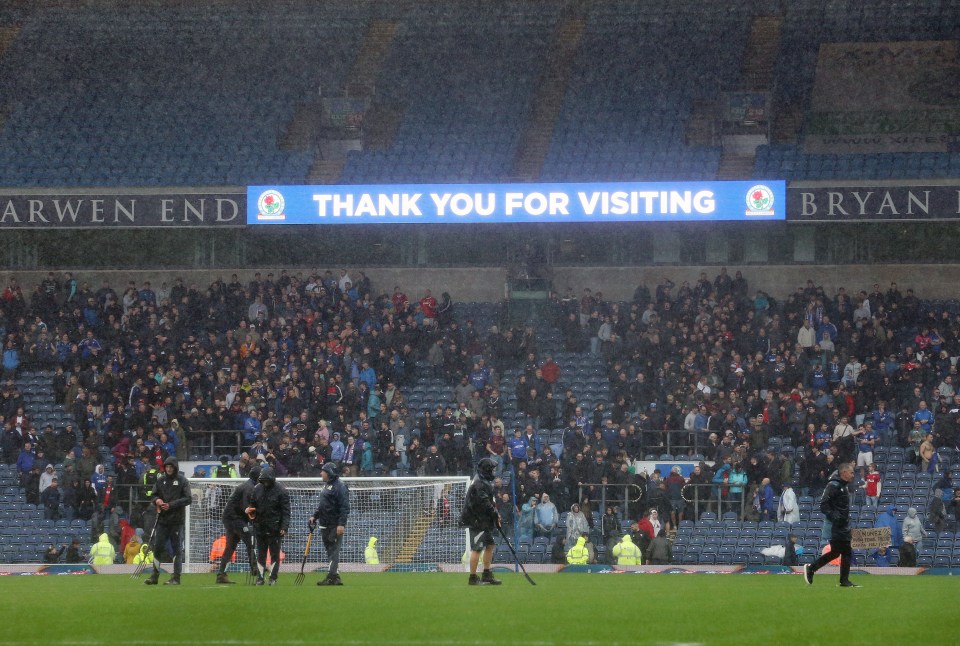 Ground staff tend to the waterlogged pitch at Ewood Park during a match between Blackburn Rovers and Ipswich Town, with a "THANK YOU FOR VISITING" sign visible in the stadium.
