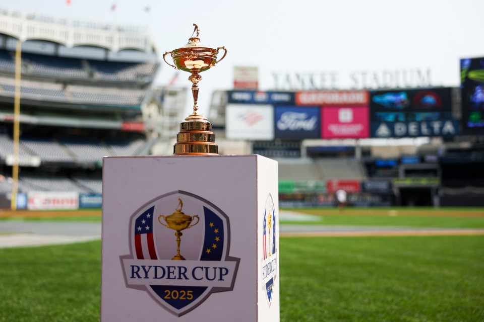 Ryder Cup trophy on a white stand with the Ryder Cup 2025 logo on a baseball field.