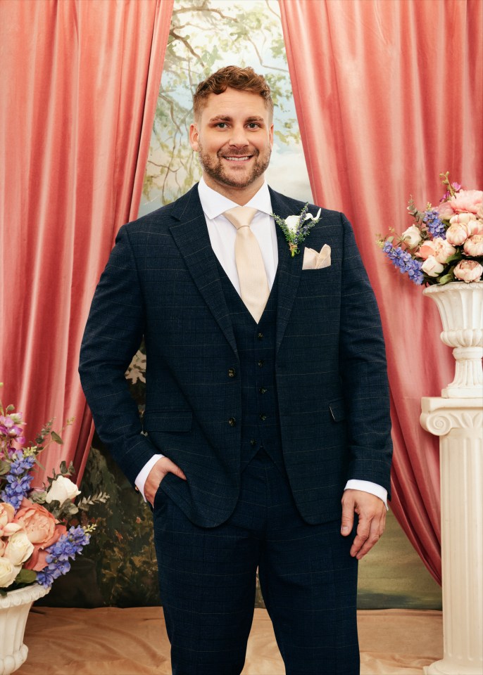 Ashley from Married at First Sight, smiling at the camera while wearing a blue suit and holding his hand in his pocket.