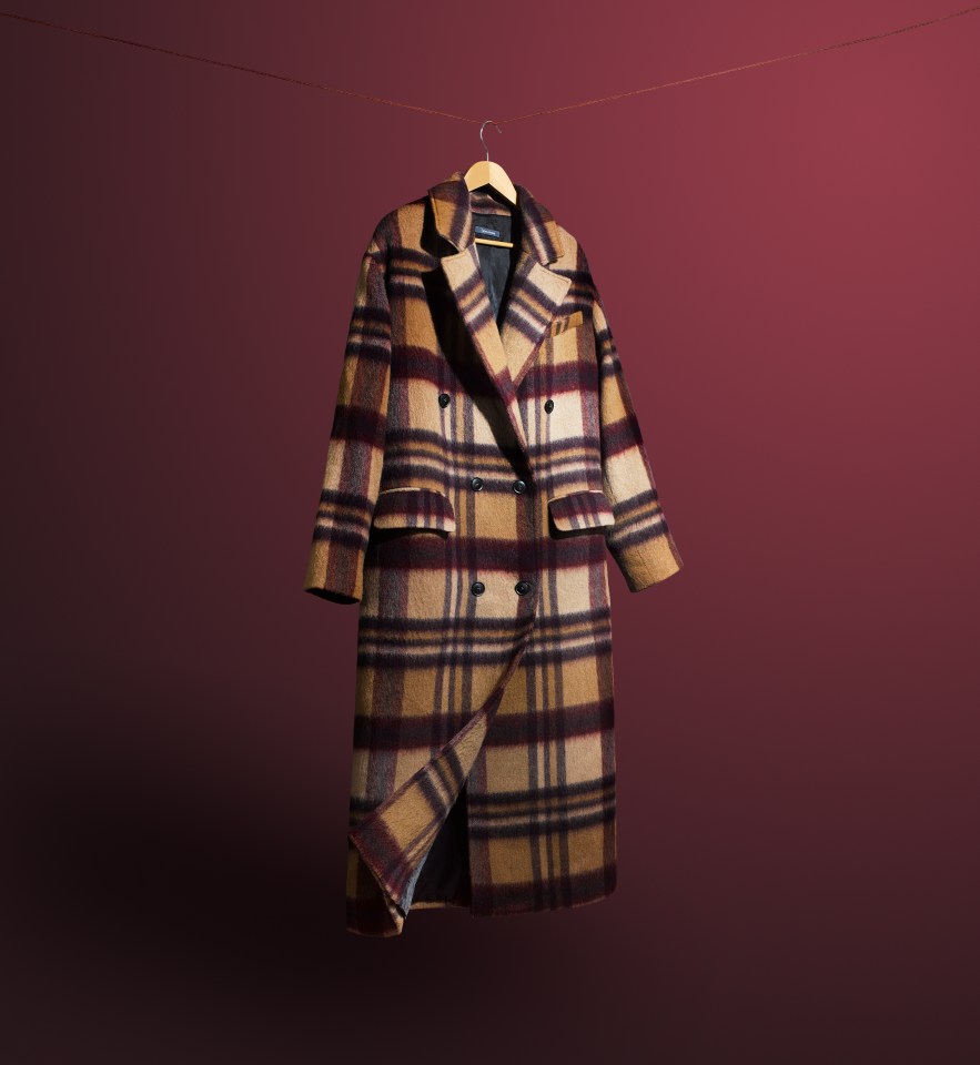 A brown, beige, and dark red plaid long coat hanging on a wooden hanger against a dark red background.