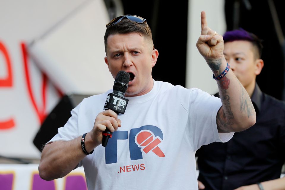 British far-right activist Tommy Robinson speaking into a microphone with his right arm raised and index finger pointing upwards.