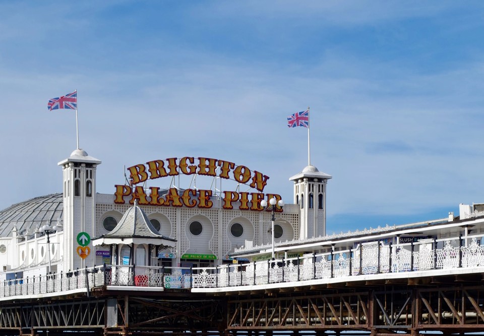 Brighton Palace Pier with seagulls on the pebble beach in the foreground and blue sky above.
