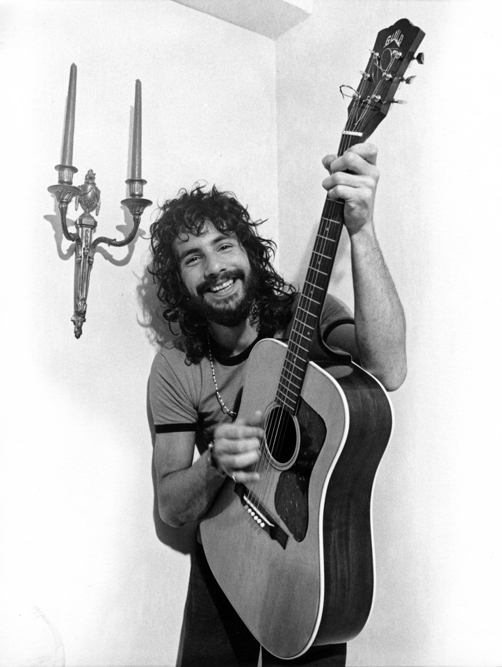 Black and white photo of Cat Stevens playing an acoustic guitar.