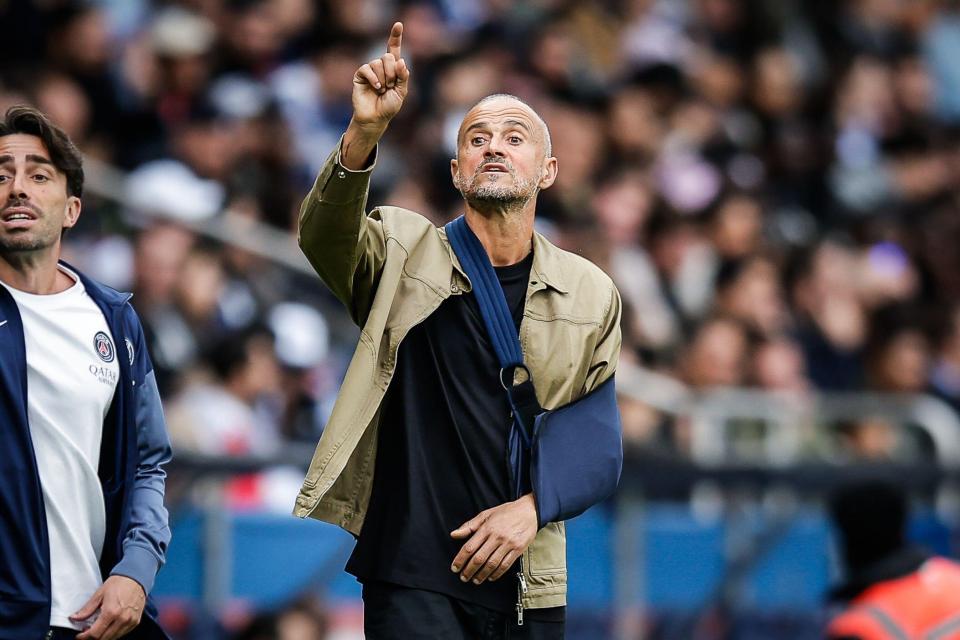Luis Enrique with his arm in a sling, pointing upwards.