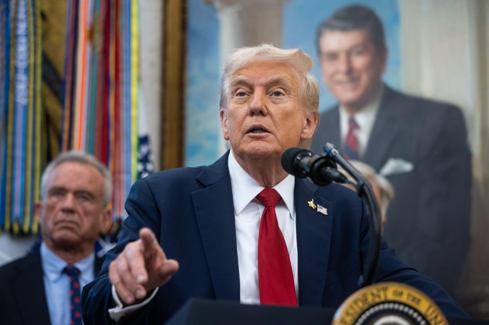 US President Donald J Trump speaking at a podium with Robert F. Kennedy, Jr. looking on.