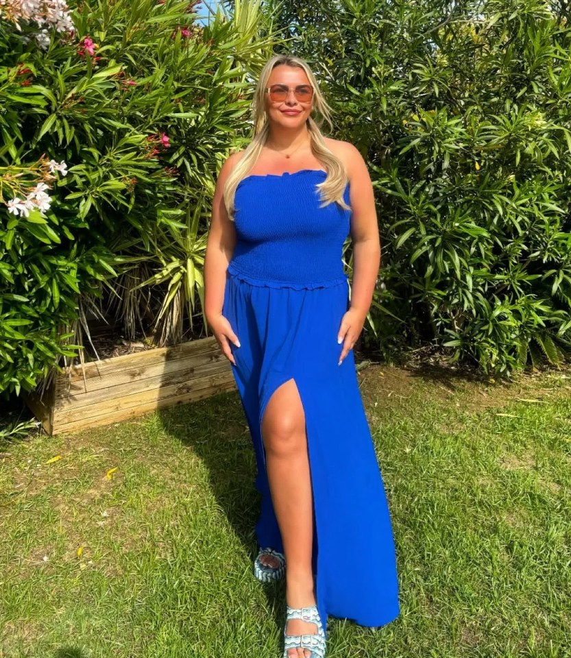 Saffron in a blue maxi dress standing in a garden.