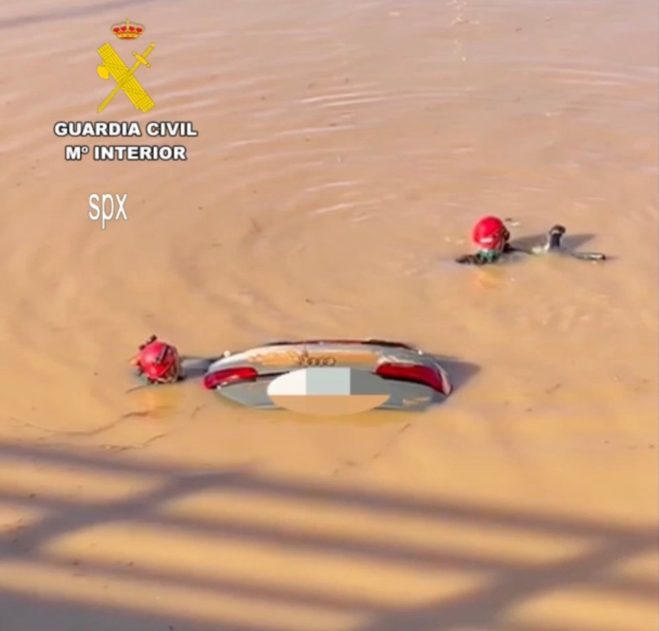 Submerged vehicle with the back half and two red helmets visible in murky floodwaters.