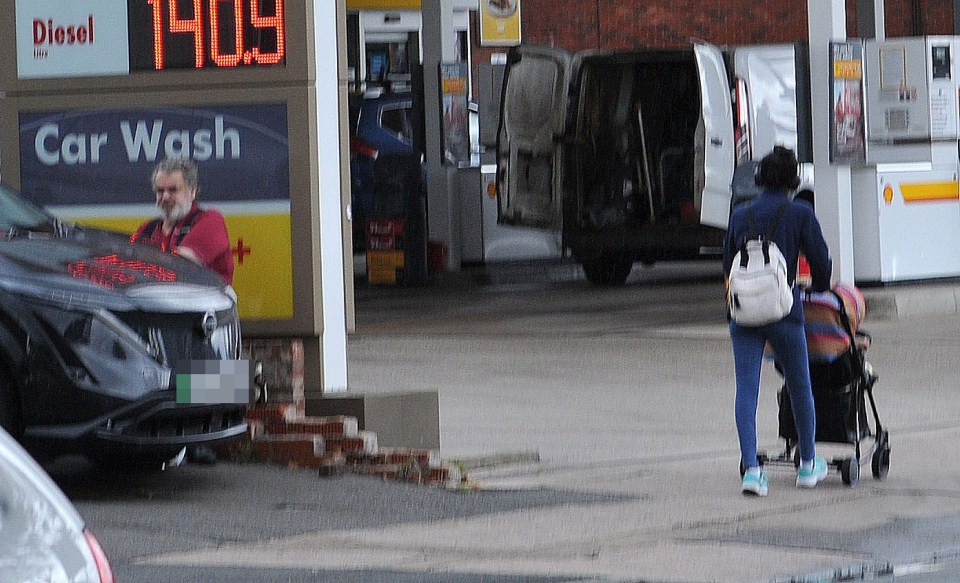 Brian Wilkinson at a petrol station in the North of England, with a person pushing a stroller in the foreground.