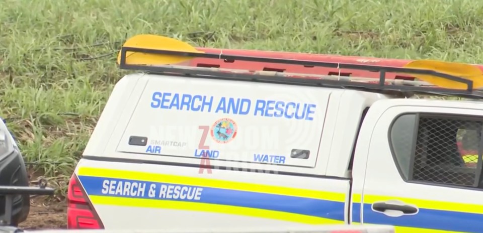 A white search and rescue vehicle with paddles on its roof, surrounded by tall grass.