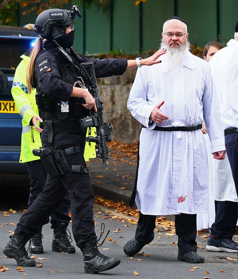 Armed police officer directing Rabbi Daniel Walker outside a synagogue after an attack.