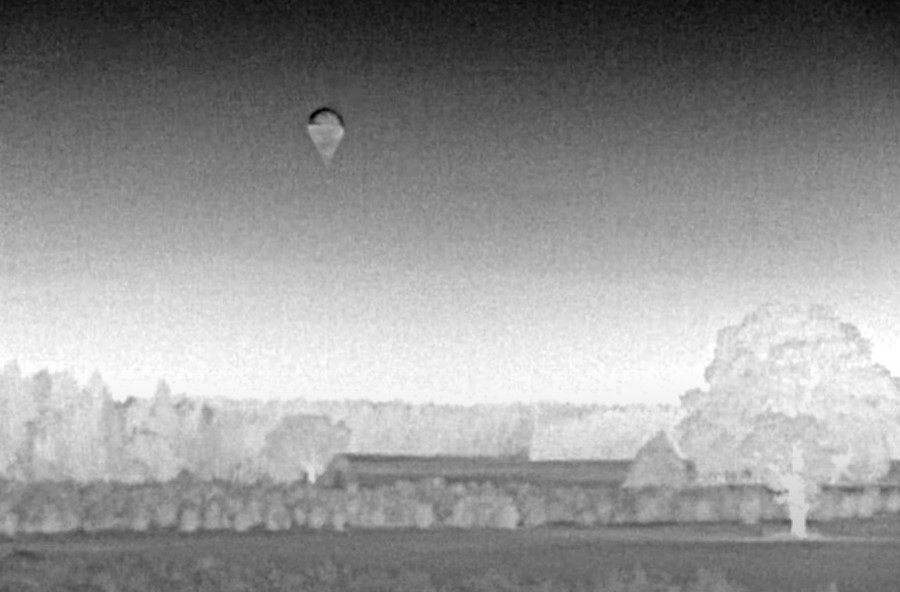 Infrared image of a small hot air balloon in the sky above a rural landscape.