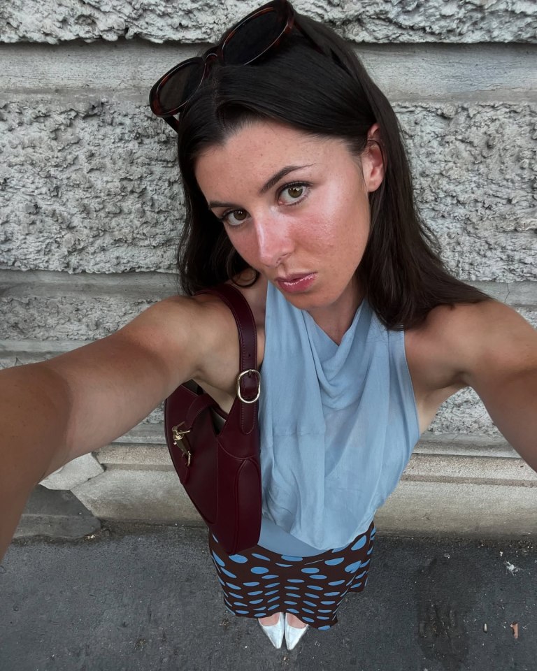 Amy Hunt in a light blue top and patterned skirt with a red handbag.