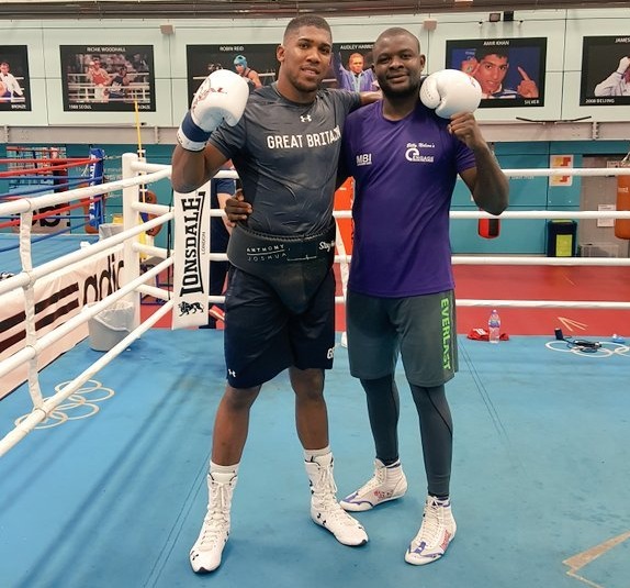 Anthony Joshua and a man in a purple shirt standing in a boxing ring.