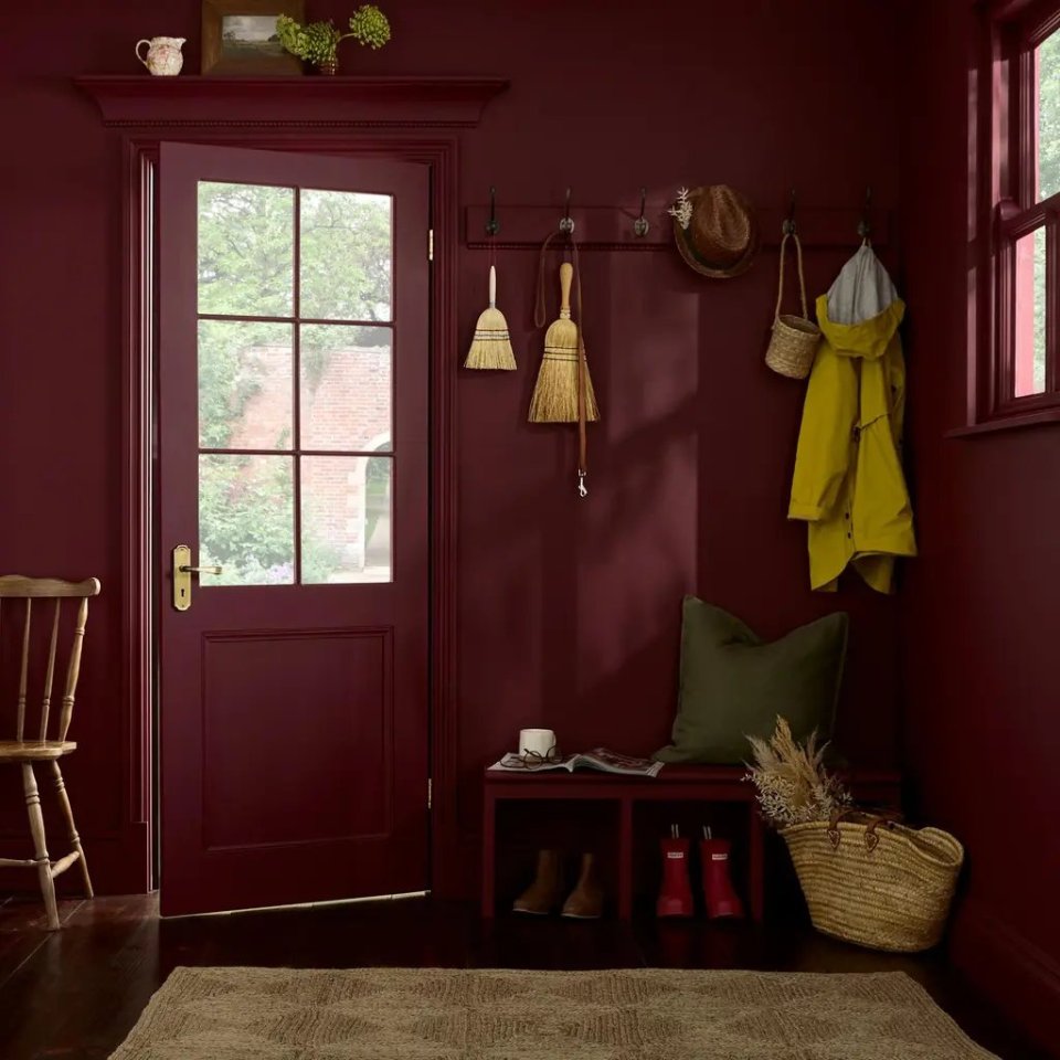An entryway painted in dark red with a bench, coat hooks, and a half-glass door.