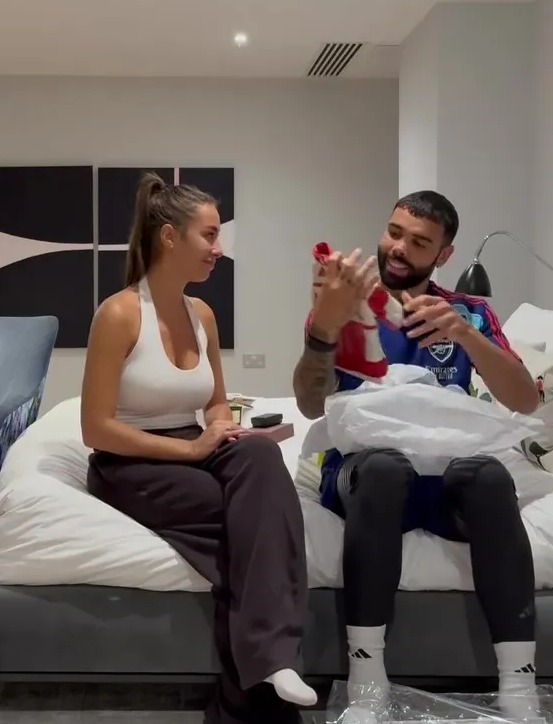 David Raya opens a gift of baby shoes while his partner sits next to him.