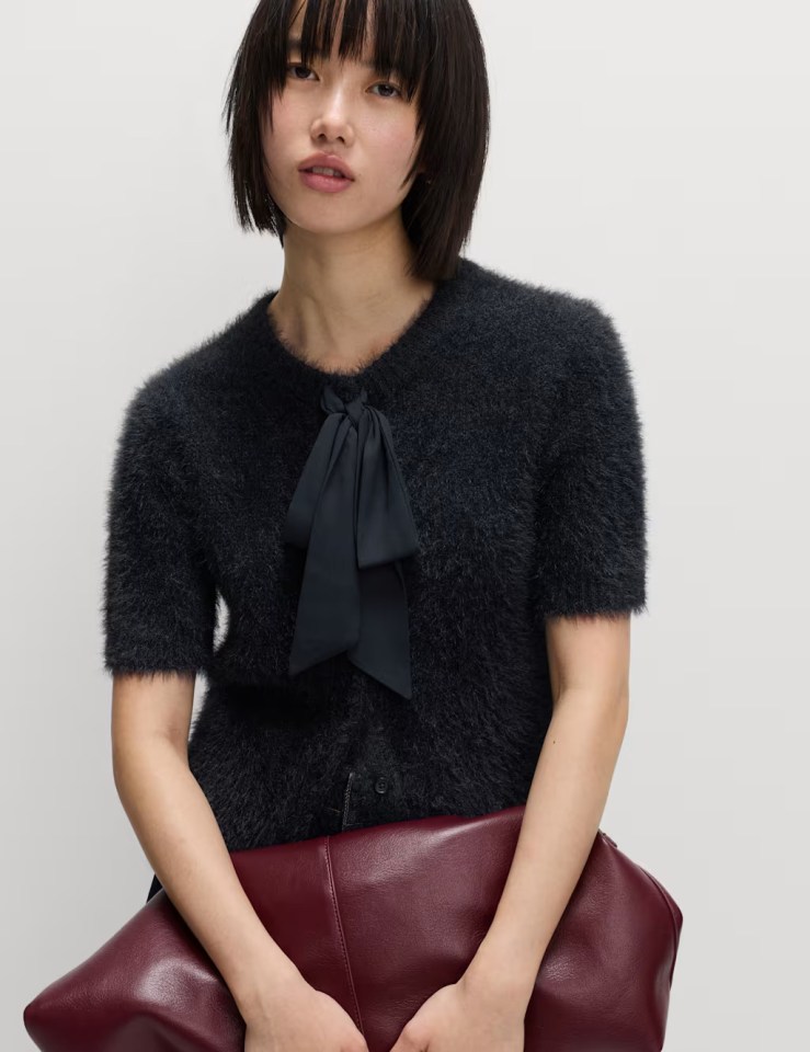Woman in a fluffy dark blue cardigan with a bow at the neck, holding a burgundy clutch.