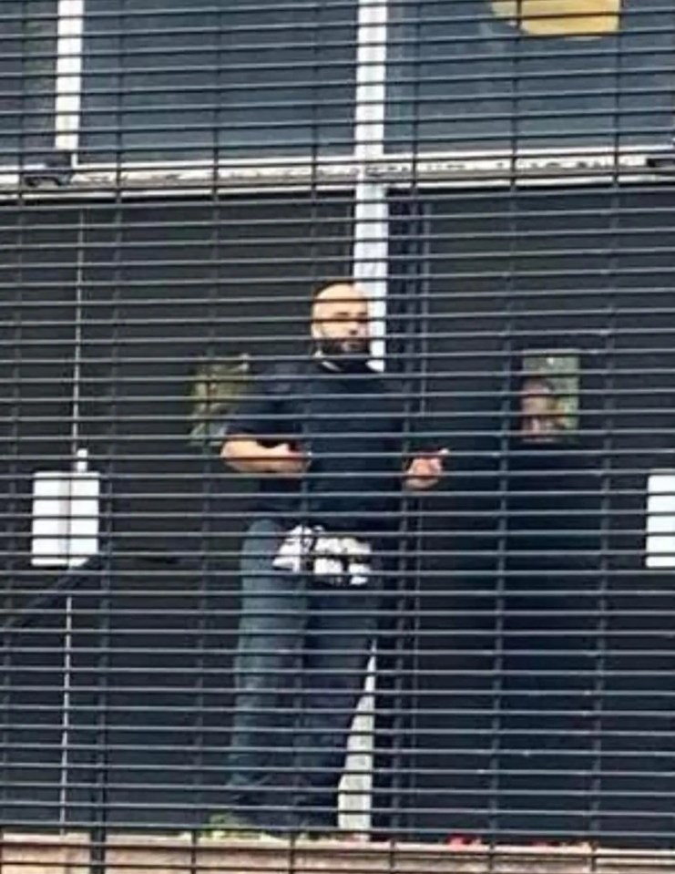 A man with a beard stands behind metal security gates, believed to be the possible Manchester Synagogue attacker.