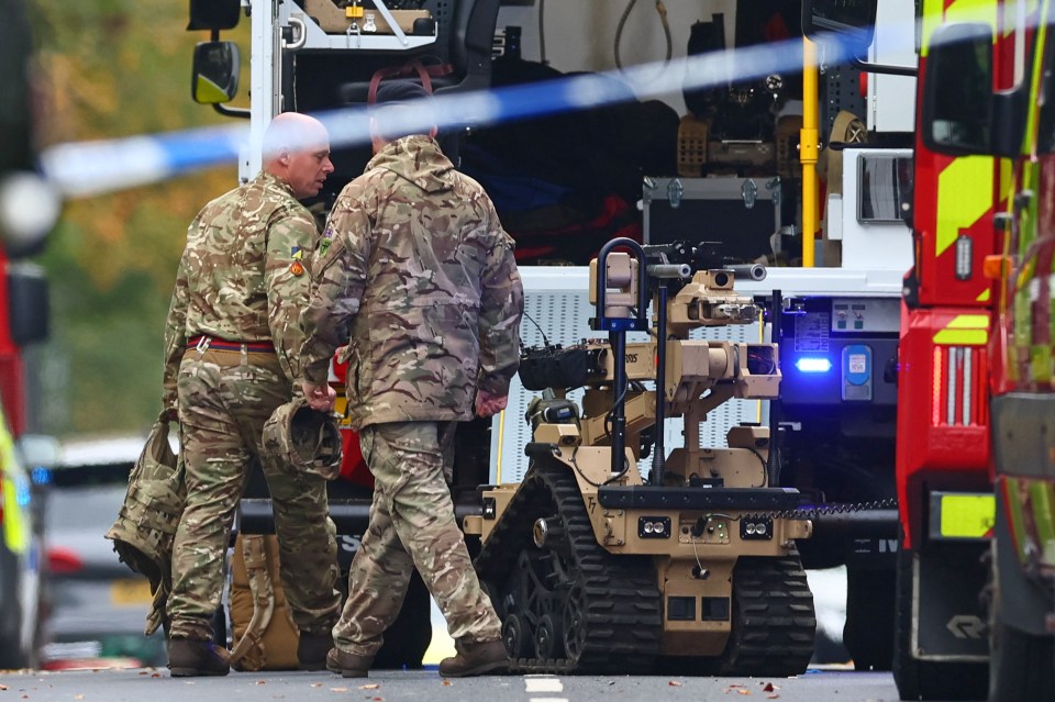 Two armed forces members in camouflage uniforms next to a bomb disposal robot.