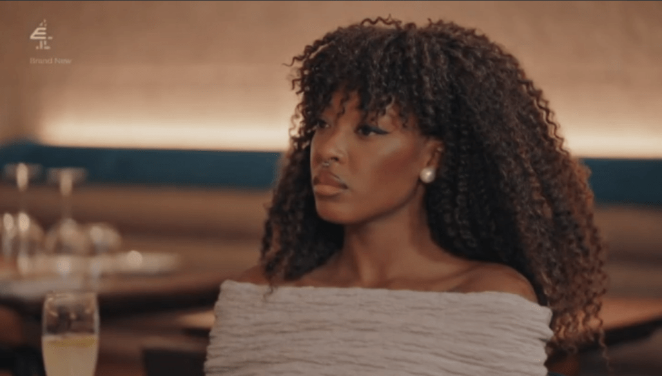 A dark-skinned woman with curly hair looks intently to her right in a restaurant setting.