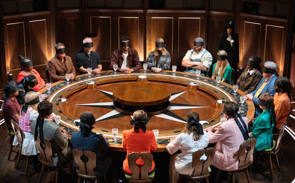People wearing blindfolds around a large circular wooden table.