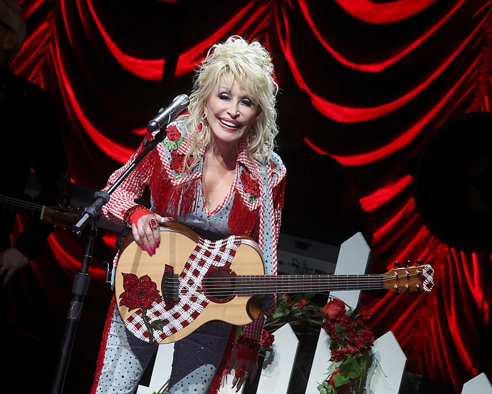 Dolly Parton performing on stage with a rhinestone-studded guitar and matching outfit.