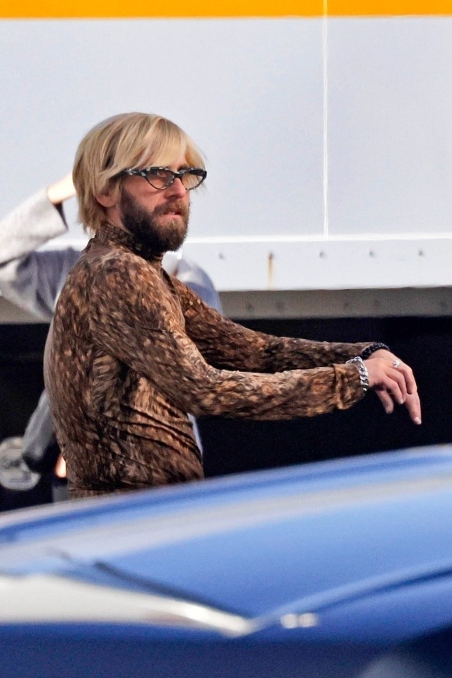 Jonah Hill in a leopard print top with shaggy blonde hair and a beard, wearing glasses.