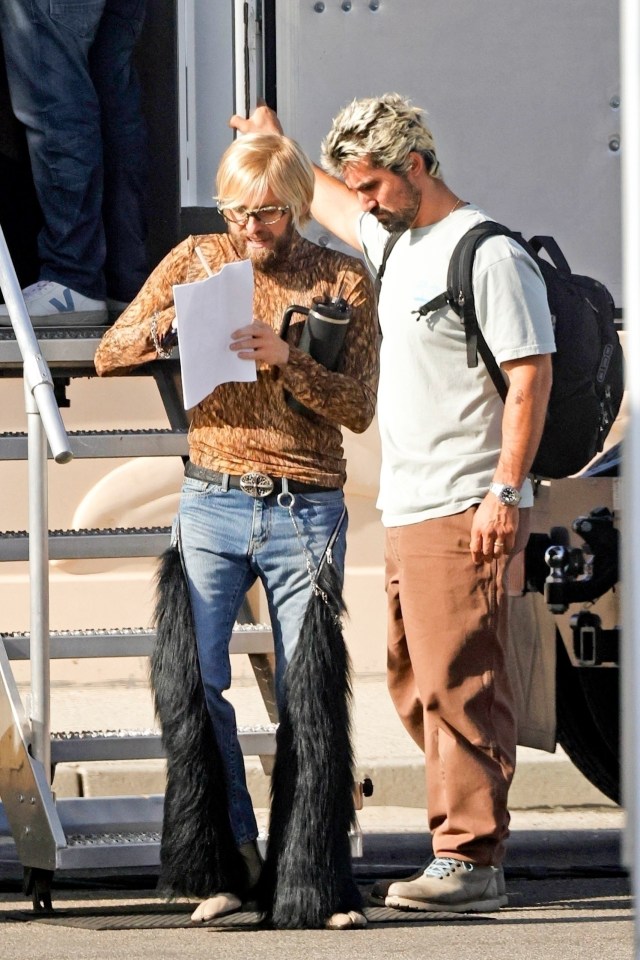 Jonah Hill in a blonde wig, leopard print top, jeans with black fringe, and sunglasses, looking at a script with another person.