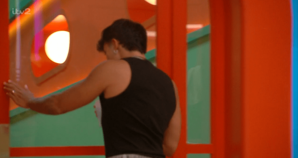 A person in a black tank top and earrings from behind, walking past colorful walls.