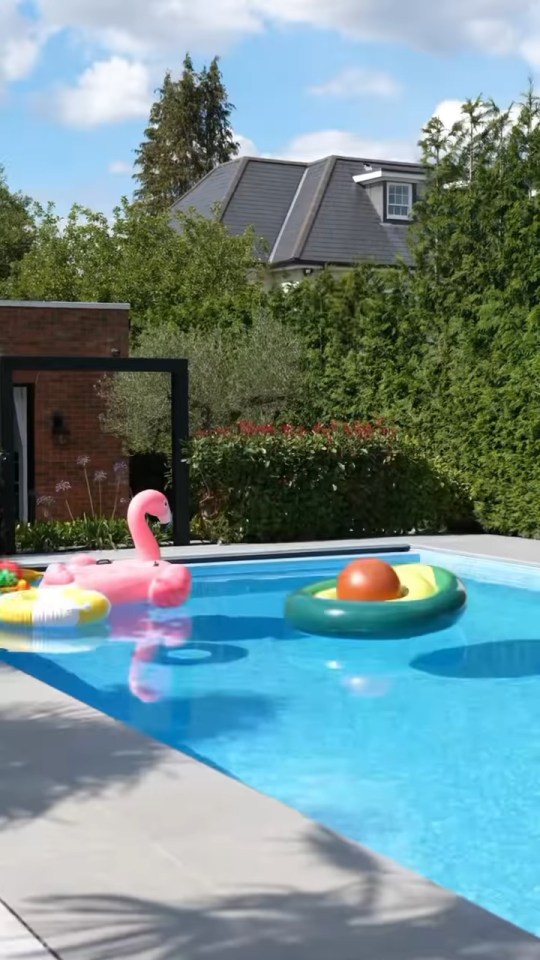 A bright blue swimming pool with a pink flamingo float, an avocado float, and a yellow and white striped ring float.