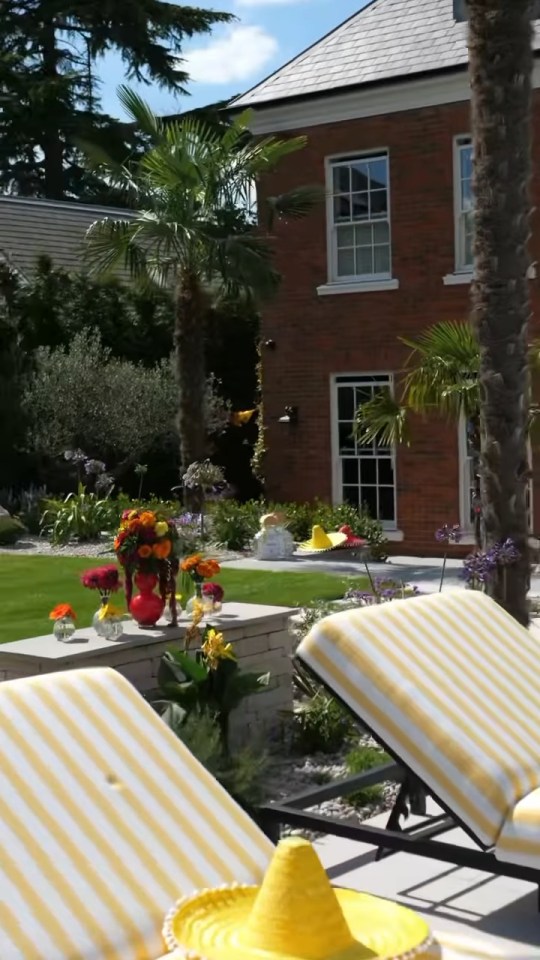 Backyard of a brick mansion with a pool, lounge chairs, and palm trees.