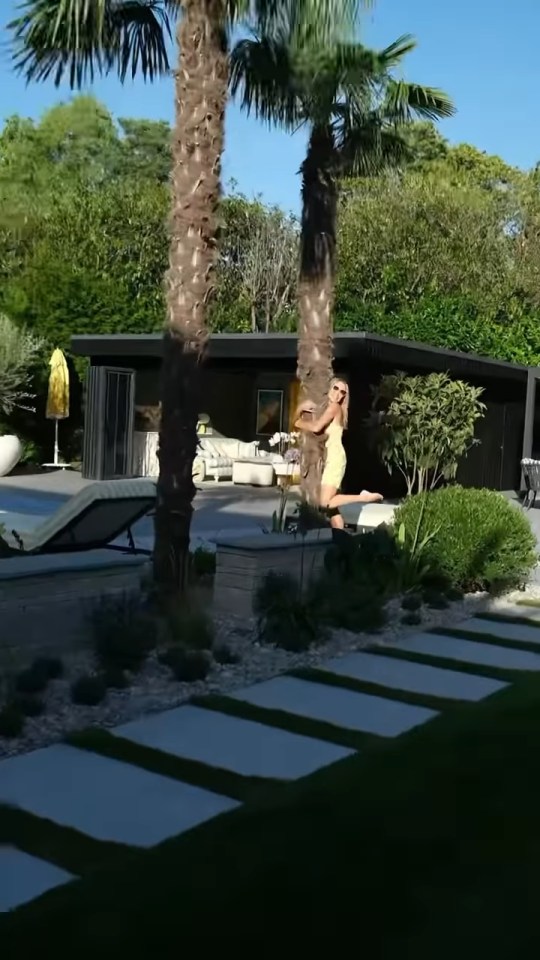 Amanda Holden posing in her garden by a palm tree with a pool house in the background.