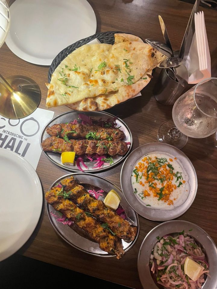 Various kebab dishes with naan bread and sides on a wooden table at Muhgli restaurant.