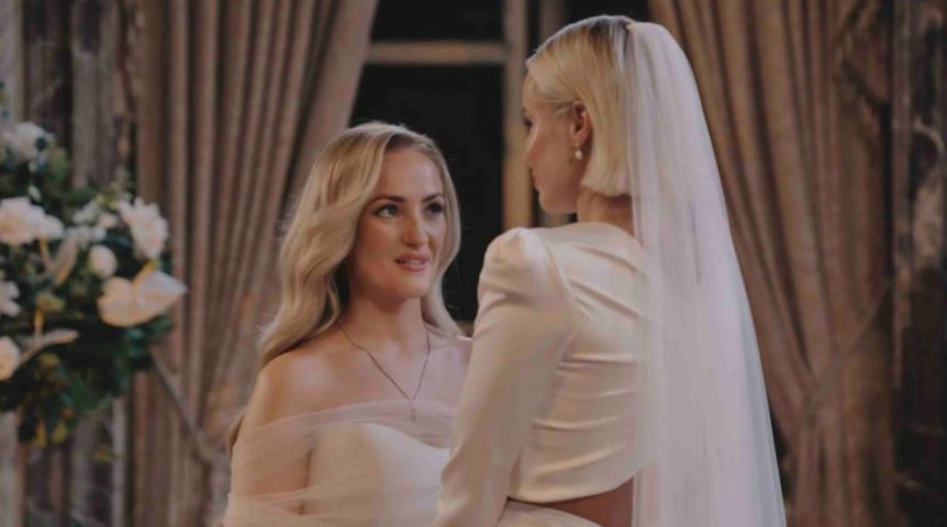 Two brides on their wedding day, one with a veil looking at the other.