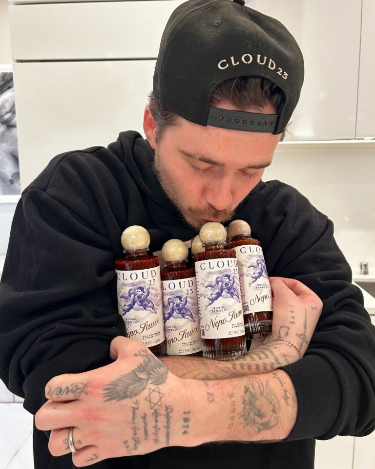 Brooklyn Beckham holding multiple bottles of "Cloud 23 Nepo Sauce" and kissing one of them.