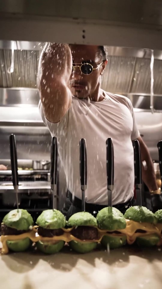 Salt Bae sprinkling salt on a row of avocado burgers.