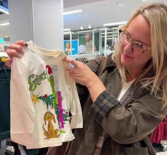 A person holding a white Grinch long-sleeved shirt with a price tag on it in a store.