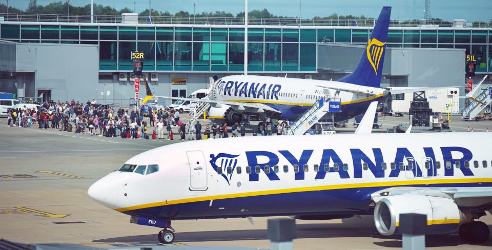 Passengers queuing on the tarmac to board a Ryanair plane at Stansted Airport, with another Ryanair plane in the foreground.