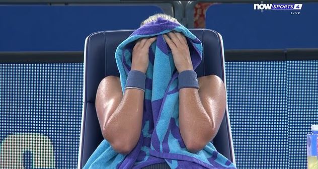 Mirra Andreeva sits on a chair with a blue and purple towel over her head and face.