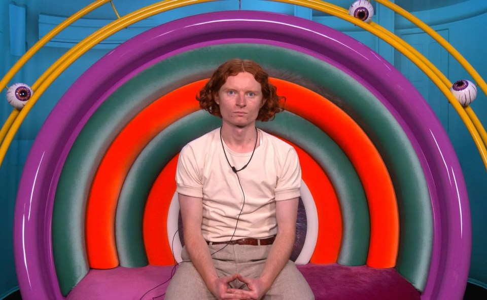 George, a contestant on Big Brother, sitting in the diary room with a rainbow-colored chair.