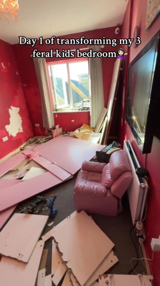 A messy bedroom with pink walls, a window, a television, a pink armchair, and scattered pink and white furniture pieces.