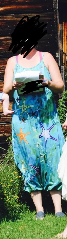 An officiant in a blue sundress with starfish patterns and visible pink bra straps, holding papers, standing in grass.