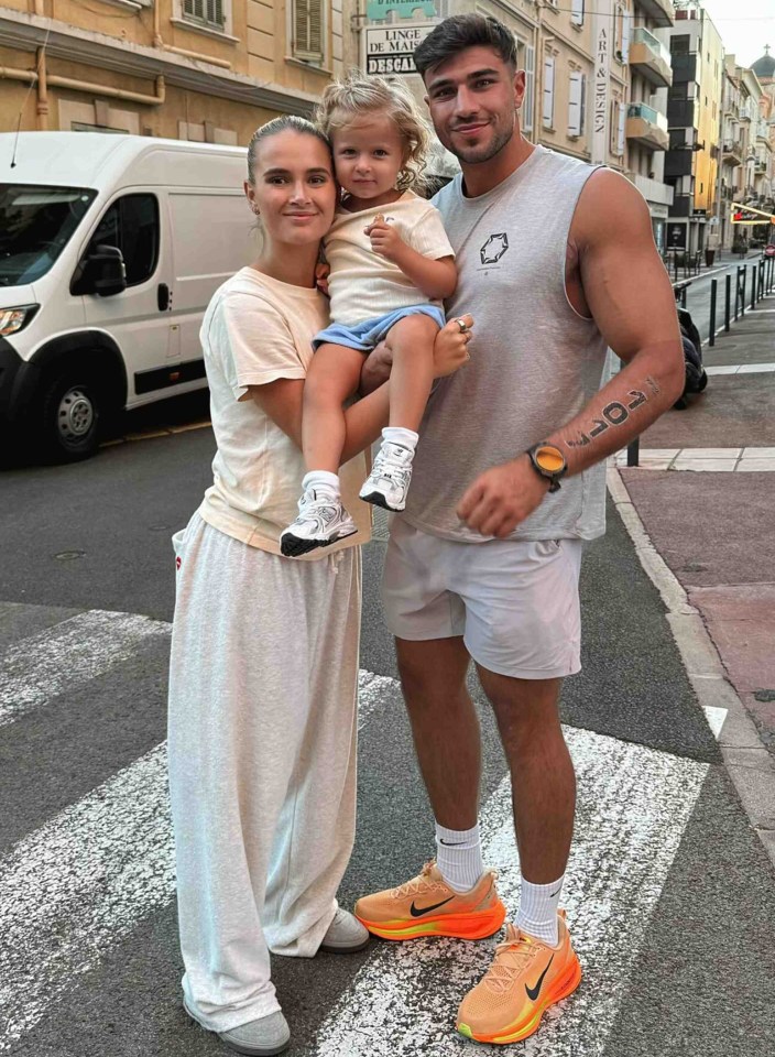 Molly-Mae Hague, Tommy Fury, and their daughter Bambi pose for a photo on a street.