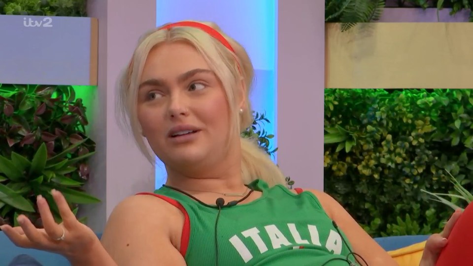 A woman in a green top with "ITALIA" written on it and a red headband, looking to her right with an ambiguous expression.