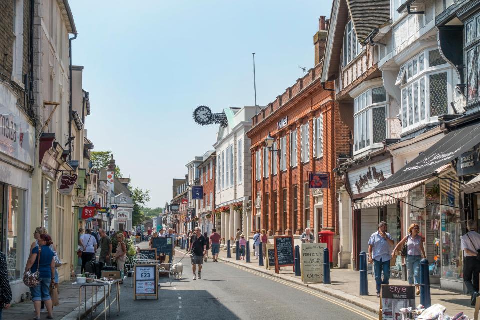 Busy High Street in Hythe, Kent, England with shops, restaurants, and a clock on a building.