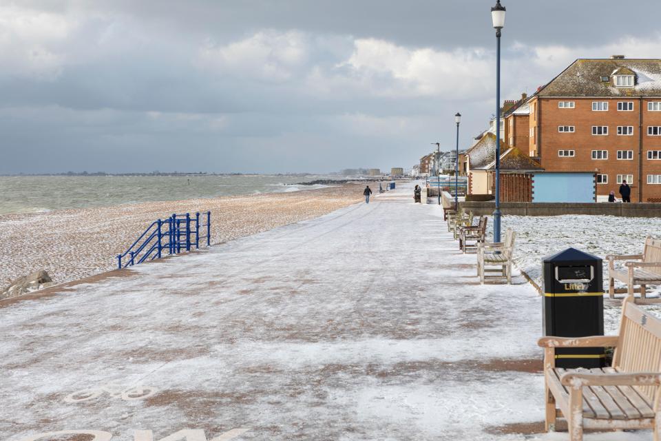 A snowy Marine Parade in Hythe, Kent, with a beach and sea to the left and buildings to the right.