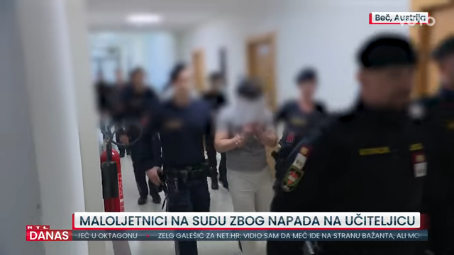 A blurred image of a young man, head covered, being escorted by police officers in a hallway.